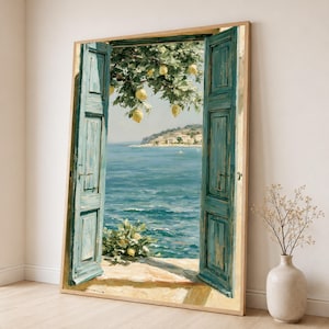 May include: A framed wall art print depicting an open pair of teal wooden shutters looking out onto a calm blue sea. A lemon tree with yellow fruit hangs over the view, and a distant coastline is visible under a clear sky, all in a light wood frame.