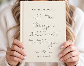 Könnte beinhalten: Ein cremefarbenes Hardcover-Notizbuch mit schwarzem Text, der lautet: A LITTLE RECORD OF all the things i still want to tell you, gefolgt von einem kleinen Herzsymbol und dem Text Love, Hannah, zentriert am unteren Rand des Einbands.