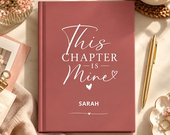 Könnte beinhalten: Ein altrosa Notizbuch mit festem Einband und dem in Weiß aufgedruckten Text "This Chapter Is Mine" in einer Mischung aus Schreib- und Serifenschrift, ergänzt durch ein kleines Herzsymbol und den Namen "SARAH" unter dem Titel.