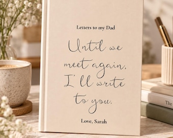 Könnte beinhalten: Ein cremefarbenes Notizbuch mit festem Einband und schwarzem Text: Letters to my Dad, Until we meet again, I'll write to you, Love, Sarah. Das Buch steht aufrecht auf einer Oberfläche, neben einer Tasse und Stiften.