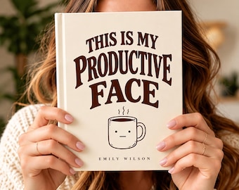 Könnte beinhalten: Ein cremefarbenes Hardcover-Buch mit dunkelbraunem Text, der THIS IS MY PRODUCTIVE FACE lautet. Unter dem Text befindet sich eine einfache Strichzeichnung einer Kaffeetasse mit neutralem Gesichtsausdruck und aufsteigendem Dampf. Der Name Emily Wilson steht unten.