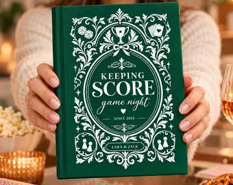 Könnte beinhalten: Ein dunkelgrünes Hardcover-Buch mit weißen, verzierten Filigranrändern und spielbezogenen Symbolen. Das Cover zeigt den Text KEEPING SCORE game night, SINCE 2026 und LARA & JACK, umrahmt von Illustrationen von Würfeln, Karten und Spielfiguren.