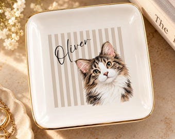 Könnte beinhalten: Eine quadratische weiße Keramikschale mit goldenem Rand. In der Mitte befindet sich eine Grafik einer braun-weißen getigerten Katze neben dem in schwarzer Schreibschrift geschriebenen Namen Oliver auf einem Hintergrund mit beigen Streifen.
