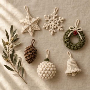 Puede incluir: Una colección de seis adornos de ganchillo que incluye una estrella crema, un copo de nieve crema, una corona verde con un lazo crema y bayas rojas, una piña marrón, una bola texturizada crema y una campana crema, junto a una rama de olivo.