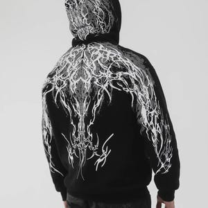 Könnte beinhalten: Ein schwarzer Kapuzenpullover mit einem komplexen, weißen und grauen Grafikdruck, der sich von der Kapuze über die Schultern bis zum Rücken erstreckt. Das Design besteht aus scharfen, miteinander verbundenen Linien und abstrakten Formen.