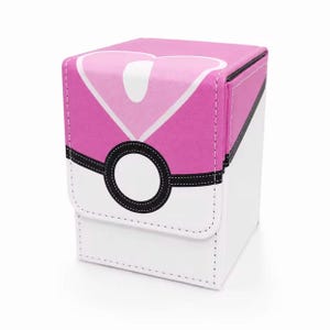 May include: A rectangular deck box featuring a pink and white color scheme with a stylized heart graphic on the top flap. The front includes a black circular emblem with a white center, mimicking a spherical design with stitched edges.