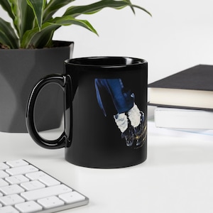 K&ouml;nnte beinhalten: Schwarze Keramik-Tasse mit einer Grafik einer behandschuhten Hand in einer blauen Jacke. Die Hand tr&auml;gt einen wei&szlig;en Handschuh mit goldenen Akzenten. Die Tasse hat einen schwarzen Henkel und ein schwarzes Innenleben.