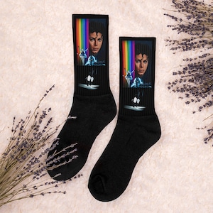 May include: A pair of black socks with a colorful rainbow design and a portrait of Michael Jackson. The socks feature a graphic of Michael Jackson performing a dance move.