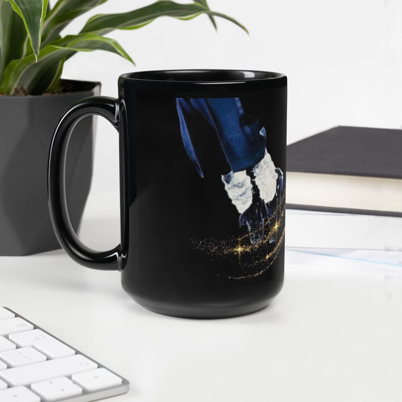 K&ouml;nnte beinhalten: Schwarze Keramik-Tasse mit einem Design eines Beins in einer wei&szlig;en Socke und einem schwarzen Schuh, mit einer blauen Jacke. Das Design ist vor einem schwarzen Hintergrund mit goldenen Glitzerakzenten. Die Tasse hat einen schwarzen Griff.