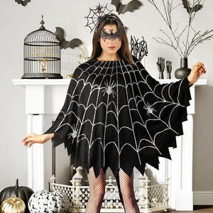 May include: A black poncho featuring a silver glitter spiderweb pattern with multiple spider graphics. The garment has a jagged, uneven hemline. It is paired with a black lace eye mask and a headband adorned with a spiderweb and spider motif.