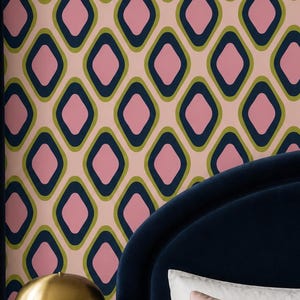 May include: Wallpaper featuring a repeating geometric pattern of rounded squares in pink, olive green, and dark navy blue on a light pink background. The design covers the wall behind a dark blue velvet headboard and a wooden nightstand.