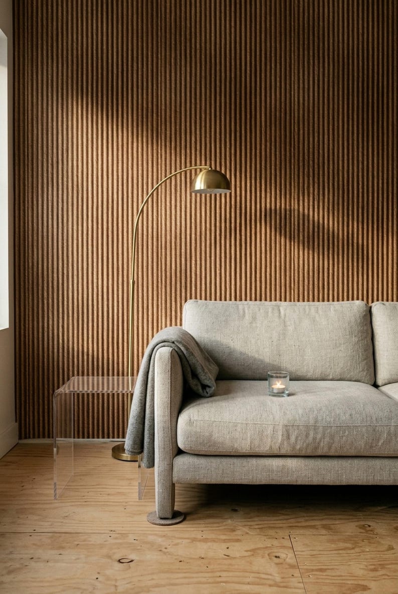May include: A light gray upholstered sofa with a matching gray throw blanket draped over the arm, a clear acrylic side table, and a gold-toned arched floor lamp. A small glass candle holder with a lit tea light sits on the sofa cushion.