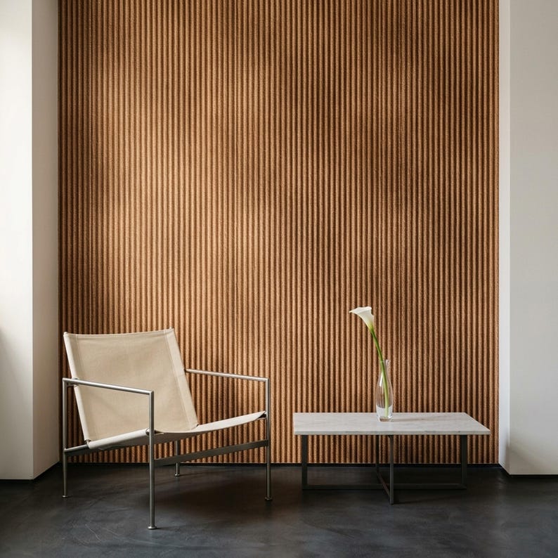 May include: A lounge chair with a cream-colored fabric seat and a thin metal frame, positioned next to a rectangular stone-topped coffee table with a metal base. A single white calla lily in a glass vase sits on the table against a ribbed wall.