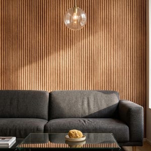May include: A dark gray sofa sits in front of a wall with vertical brown ribbed paneling. A glass coffee table holds a small beige bowl with a natural sponge. A clear, spherical glass pendant light with a brass fixture hangs from the ceiling.