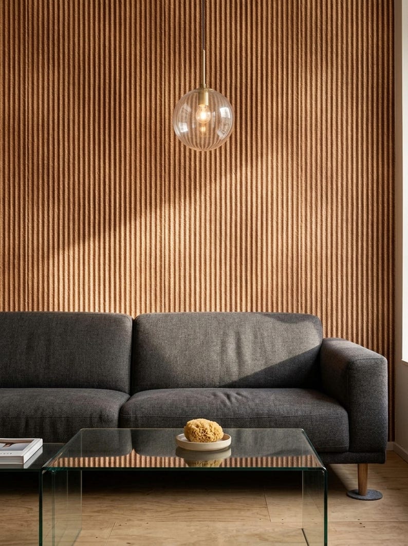 May include: A dark gray sofa sits in front of a wall with vertical brown ribbed paneling. A glass coffee table holds a small beige bowl with a natural sponge. A clear, spherical glass pendant light with a brass fixture hangs from the ceiling.