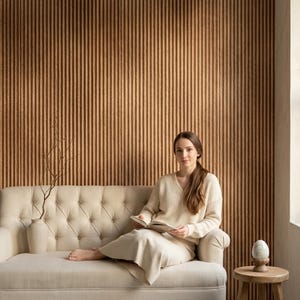 May include: A cream-colored tufted sofa with a matching sweater and skirt, a beige vase with a bare branch, and a small wooden stool holding a smooth white stone egg, all set against a vertical ribbed brown wall paneling background.