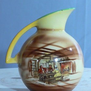 May include: A brown and yellow ceramic pitcher with a green rim. The pitcher has a scene painted on it of three people sitting at a table in a room with a fireplace.