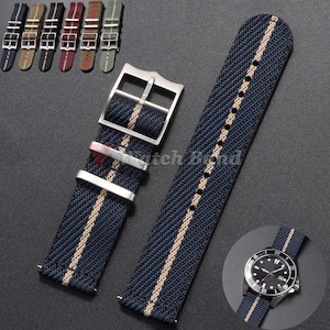 Puede incluir: Una correa de reloj tejida en azul marino con una franja vertical central de color beige, una hebilla de metal plateado y dos trabillas plateadas a juego. Un recuadro circular muestra la correa unida a un reloj analógico de esfera negra.