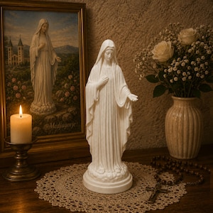 Könnte beinhalten: Eine weiße, matte Statue der Jungfrau Maria, die auf einem wolkenförmigen Sockel steht. Sie trägt ein drapiertes Gewand und eine Kopfbedeckung. Eine Hand liegt auf der Brust, die andere ist ausgestreckt. Die Figur besteht aus glattem Material.