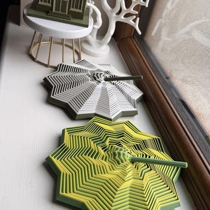 Può includere: Un modello di edificio Irish Pub stampato in 3D verde su un supporto bianco, una scultura bianca a forma di corallo e tre oggetti geometrici a forma di stella a più strati in bianco, giallo-verde e blu-arancione, con un'asta centrale.
