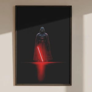 Könnte beinhalten: Ein rechteckiger gerahmter Wandkunstdruck mit einer dunklen, zentrierten Illustration einer schwarz gepanzerten Figur mit Helm und Umhang, die ein leuchtendes rotes Lichtschwert hält, das einen hellroten Schein auf den Boden wirft.