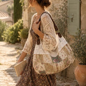 Peut inclure: Un sac à bandoulière de style hobo présentant un motif patchwork de carrés de tissu floral dans des tons vert sourd, crème et rose, agrémenté d'une large bande de dentelle blanche sur le dessus et de lanières en cuir marron foncé.