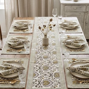 Pode incluir: Um conjunto de mesa com um caminho de mesa comprido e quatro individuais com um padrão floral repetitivo em verde-azeitona e cinzento. Cada lugar inclui um prato de cerâmica, um guardanapo de tecido estampado, talheres dourados e copos.