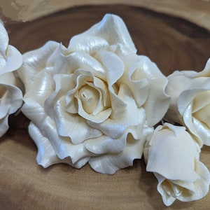 May include: Five white sugar roses with a pearl-like sheen. The roses are arranged on a wooden surface.