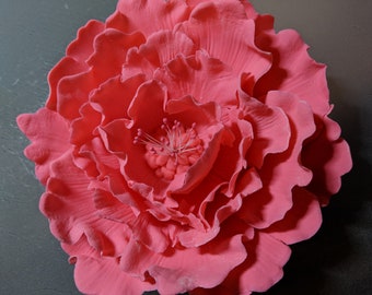 May include: A large, pink, fabric flower with a detailed center. The flower is made of many petals and has a realistic appearance.