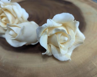 May include: Three off-white artificial roses with a slightly cream colour. The roses are arranged on a wooden surface.