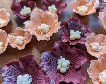 May include: Assortment of handmade sugar flowers in shades of peach and burgundy with pearl accents. The flowers are perfect for decorating cakes, cupcakes, and other desserts.