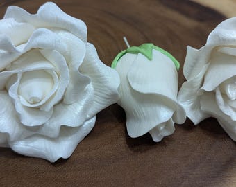 May include: Three white sugar roses, two are fully bloomed and one is a bud. The roses are on a wooden surface.