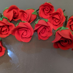 May include: A collection of 12 red felt roses with green stems. The roses are arranged in a cluster on a gray surface.