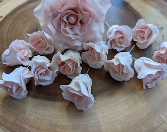 May include: A collection of 12 pink sugar roses, some with stems, on a wooden surface. The roses are various sizes and are perfect for decorating cakes or cupcakes.