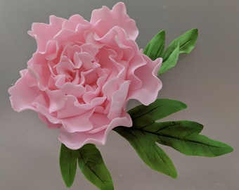 May include: A pink sugar flower with green leaves. The flower is made of fondant and is a realistic representation of a peony.