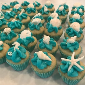 May include: A collection of mini cupcakes decorated with turquoise frosting and various white seashell and starfish toppers.