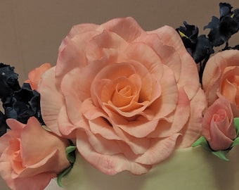 May include: A close-up of a cake decorated with pink and peach roses and blue flowers. The roses are made of fondant and have a realistic appearance.
