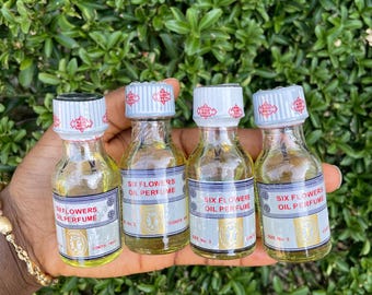 May include: Four small, clear glass bottles filled with a yellow liquid, each labeled Six Flowers Oil Perfume. The bottles feature white screw-on caps with red text and a white label with blue and gold accents, including the text Size No. 3.