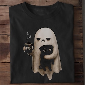 May include: A black t-shirt featuring a graphic of a white ghost with a bored expression holding a black mug with the text MEH and a wisp of steam. The ghost is embracing a small black pug dog. The design is centered on the front of the shirt.