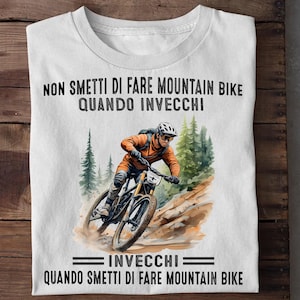 Pode incluir: Uma t-shirt branca com um gráfico em estilo aguarela de um ciclista de montanha num trilho de terra. O texto diz: NON SMETTI DI FARE MOUNTAIN BIKE QUANDO INVECCHI, e abaixo do gráfico: INVECCHI QUANDO SMETTI DI FARE MOUNTAIN BIKE.