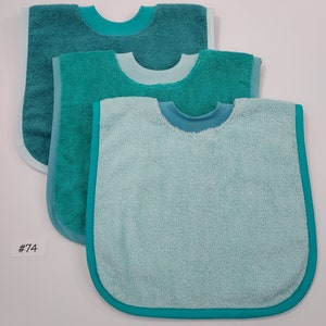 May include: Three turquoise terrycloth baby bibs with a turquoise trim. The bibs are layered on top of each other, with the largest bib on the bottom and the smallest bib on top. The bibs are all the same design, with a rounded neckline and a pointed bottom.