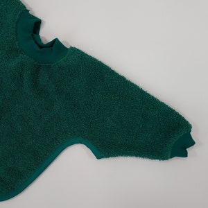 May include: A dark green fuzzy sweatshirt with a high neck and long sleeves.