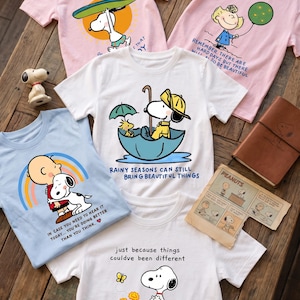 以下が含まれることがあります： ピーナッツのキャラクターが描かれた5枚のTシャツ：サーフィンをするスヌーピーのピンクのシャツ、サリーと風船のピンクのシャツ、傘に入ったスヌーピーの白いシャツ、チャーリー・ブラウンとスヌーピーの青いシャツ、スヌーピーと花が描かれた白いシャツ。