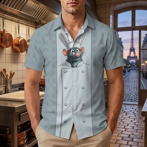 May include: A light blue short-sleeved button-down shirt featuring a central graphic of a cartoon rat wearing a white chef hat and uniform. The shirt has a repeating pattern of small chef hats and cheese wedges across the light blue fabric.