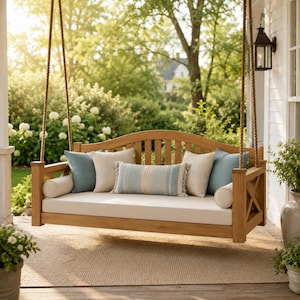May include: A wooden porch swing featuring a natural finish, suspended by thick ropes. The swing includes a long cream-colored seat cushion, two round bolster pillows, two square light blue pillows, two square beige pillows, and a striped lumbar pillow.