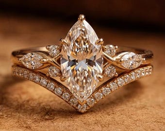 May include: A gold ring set featuring a central marquise-cut stone flanked by smaller marquise and round stones, paired with a V-shaped band encrusted with numerous tiny round stones along the entire outer edge of the chevron design.