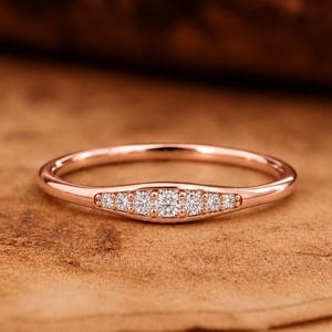 Peut inclure: Une bague en or rose dotée d'un anneau fin et d'un sertissage central incurvé orné de cinq petites pierres rondes transparentes disposées en rangée horizontale, la pierre centrale étant légèrement plus grande que les quatre autres.