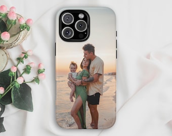 Puede incluir: Una funda rectangular para smartphone con la fotografía impresa de una familia de tres personas en una playa de arena al atardecer. La imagen muestra a una persona con un vestido verde sosteniendo a un bebé junto a otra con camiseta beige.
