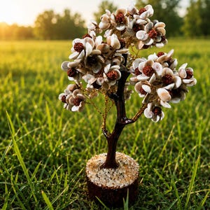 Puede incluir: Una escultura de árbol decorativa con un tronco marrón oscuro y ramas hechas de alambre dorado fino. Las ramas están adornadas con pequeñas flores de conchas blancas y semillas redondas de color marrón rojizo. La base es un disco marrón texturizado.