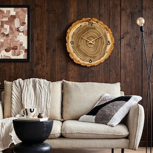 May include: A round wall clock crafted from a natural wood slice featuring visible tree rings, a rough bark edge, and thin gold-coloured hands. The clock face displays black numerals at the 12, 3, 6, and 9 o'clock positions with simple black dots for the remaining hours.